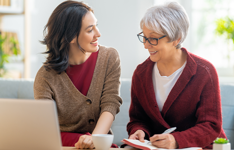 An elderly mother and her daughter look at their finances on a laptop.